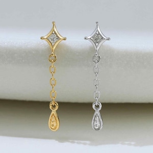 May include: Two dangling earrings, one gold-toned and one silver-toned, each featuring a four-pointed star stud with a central clear stone, a short delicate chain, and a small teardrop-shaped charm at the bottom set with a tiny clear stone.