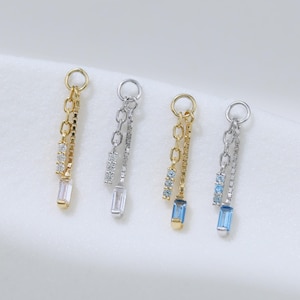 Peut inclure: Quatre breloques pendantes composées d'un petit anneau circulaire relié à une fine chaîne et d'une pierre précieuse taille baguette. L'ensemble comprend deux breloques dorées avec des pierres claires et deux argentées avec des pierres bleu clair.