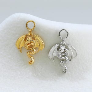 May include: Two metal dragon charms, one in a gold tone and one in a silver tone. Each charm features a detailed dragon with spread wings and a coiled tail, topped with a small circular jump ring for attachment to jewelry or other accessories.