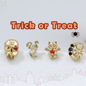 May include: Four gold-tone stud earrings featuring Halloween motifs: a skull with a red stone, a ghost with a clear stone, a bat with a red stone, and a crescent moon with a spider and black stones. The text Trick or Treat and Happy Halloween appears.