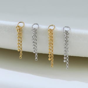 Op de afbeelding: Vier individuele oorbelbedels op een rij, afwisselend in goud- en zilverkleurige tinten. Elke bedel heeft een kleine ronde ring waaraan twee delicate hangende kettinkjes zijn bevestigd, één bestaande uit kleine kraaltjes en één uit schakels.
