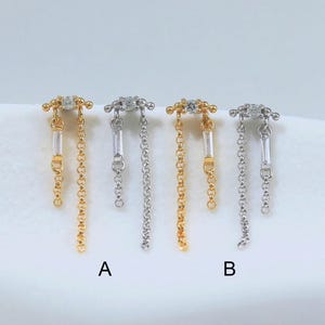 May include: Four dangling earrings arranged in a row, labeled A and B. Each earring features a small round stone at the top, a vertical baguette-cut stone, and a delicate metal chain. Two earrings are gold-toned and two are silver-toned.