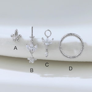 Pode incluir: Quatro peças de joalharia prateadas rotuladas A, B, C e D. O item A é um brinco de flor-de-lis. O item B é um pendente com pedras de corte marquise. O item C é uma pequena argola com um pendente. O item D é um anel circular com detalhes texturizados.
