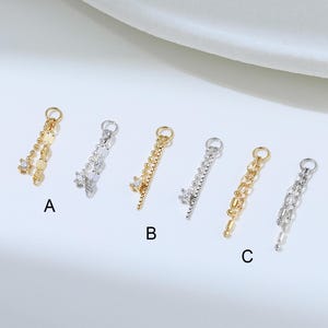 May include: Six metal charms arranged in pairs labeled A, B, and C. Each pair includes one gold-tone and one silver-tone charm. The charms feature delicate chains, small beads, and a single clear stone setting attached to a circular jump ring.