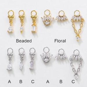 May include: A collection of gold and silver-toned metal charms featuring clear crystals. The charms are arranged in two rows, labelled Beaded and Floral, with individual pieces marked A, B, and C. Designs include teardrop, baguette, and crown shapes.