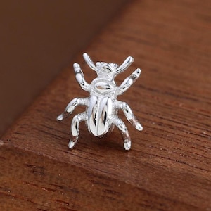 May include: A small, silver-colored insect figurine with six legs and two antennae. The detailed insect is positioned on a wooden surface, showcasing its intricate design. The figurine is a decorative item.