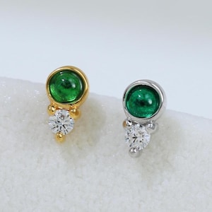 May include: A pair of stud earrings, one gold and one silver, each featuring a round, vibrant green gemstone and a cluster of small, sparkling white gemstones. The earrings are displayed on a white surface.
