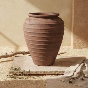Op de afbeelding: Een grote, terracotta-kleurige aardenwerken pot met een brede, ronde vorm en een dikke, opvallende rand. Het buitenoppervlak is voorzien van een reeks horizontale, getextureerde ribbels die rondom de gehele omtrek van de pot lopen.
