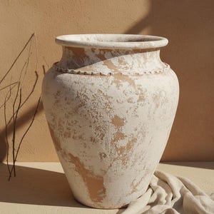 Pode incluir: Um vaso de terracota de boca larga com um acabamento branco desgastado sobre uma base de argila de cor castanha natural. O vaso tem um rebordo arredondado proeminente e uma faixa horizontal decorativa em relevo à volta do pescoço.