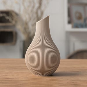 May include: A beige, ribbed vase with a distinctive, angled opening. The vase has a bulbous body and a slender neck, and it sits on a wooden table. The background is blurred, suggesting a room setting. The vase is likely for decorative purposes.