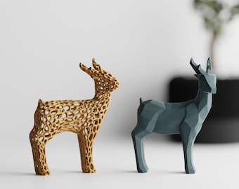 May include: Two deer figurines standing side by side. The left deer is tan with a complex, open-work, web-like lattice structure. The right deer is solid, dark blue-gray with a faceted, geometric, low-poly surface design and smooth edges.