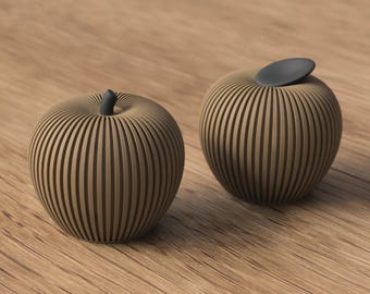 May include: Two apple-shaped decorative objects with a ribbed, tan-colored exterior. One apple features a small, dark gray stem at the top, while the other apple has a smooth, dark gray, oval-shaped indentation on its upper surface.