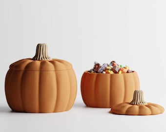 May include: Two orange pumpkin-shaped ceramic containers with ribbed textures and light beige stems. One container is closed with its lid, while the other is open and filled with assorted small candies, with its lid resting beside it.