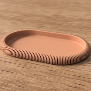 Op de afbeelding: Een perzikvormige, ovaalvormige schaal met een geribbelde rand. De schaal is gemaakt van een stevig materiaal en staat op een houten oppervlak. Het ontwerp is eenvoudig en modern, geschikt voor diverse doeleinden.