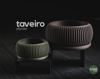 May include: Two round planters with vertical ribbed textures, one olive green and one dark brown, each resting on a black metal stand. The text "taveiro planter" appears in white, and a small green circular logo with "h3liø design" is visible.