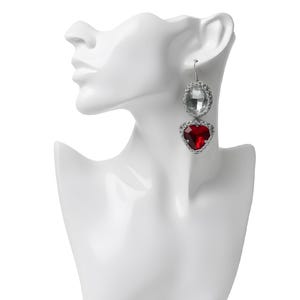 Può includere: Un paio di orecchini pendenti esposti su una testa di manichino bianca. Gli orecchini presentano una grande gemma trasparente di forma ovale sopra una gemma rossa a forma di cuore, entrambe circondate da una montatura color argento. Gli orecchini pendono da ganci color argento.