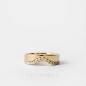 Puede incluir: Un anillo dorado con un diseño ondulado. El anillo presenta una fila de pequeñas piedras preciosas transparentes a lo largo de la curva inferior. La banda es gruesa y lisa, con el texto "fairydiamjewel" en la parte inferior.