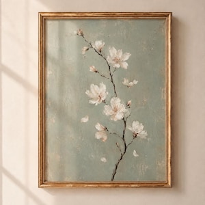 May include: A framed wall art print featuring a delicate branch with white cherry blossoms against a textured, muted sage green background. The artwork is encased in a thin, weathered gold-toned frame with visible distressed detailing.