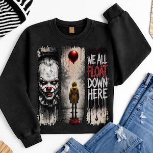 May include: A black crewneck sweatshirt featuring a graphic print with a clown face on the left, a figure in a yellow raincoat holding a red balloon in the centre, and the text WE ALL FLOAT DOWN HERE in white and red with a dripping paint effect.