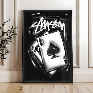 May include: A framed vertical poster featuring a glossy black background with a white, stylized graffiti-style logo at the top. Below the logo, two playing cards, an ace of spades and a king of spades, are depicted with a 3D liquid effect.