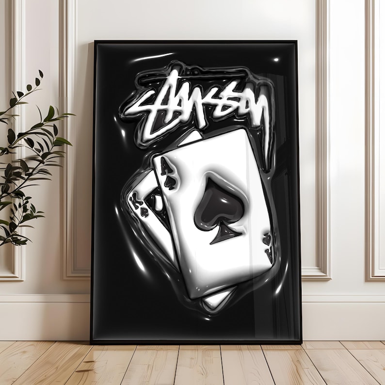 May include: A framed vertical poster featuring a glossy black background with a white, stylized graffiti-style logo at the top. Below the logo, two playing cards, an ace of spades and a king of spades, are depicted with a 3D liquid effect.