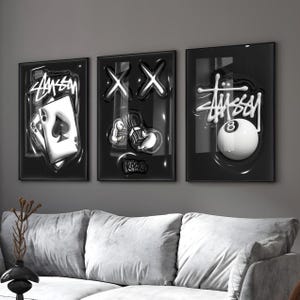 May include: A set of three black framed wall art prints featuring glossy, raised-effect graphics. The left print shows an ace of spades playing card with Stussy text. The center print displays X eyes and cartoon hands. The right print shows an 8 ball.