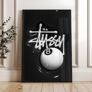 May include: A rectangular framed wall art piece featuring a glossy black background with a raised, three-dimensional white St&uuml;ssy logo script positioned above a large, white billiard ball with a black number eight centered on its surface.