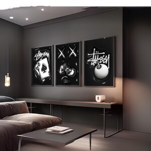 May include: Three rectangular wall art prints featuring black backgrounds with white graphic designs. The left print shows an ace of spades playing card with Stussy text. The center print displays two X symbols and a stack of cash. The right print features an eight ball with Stussy text.