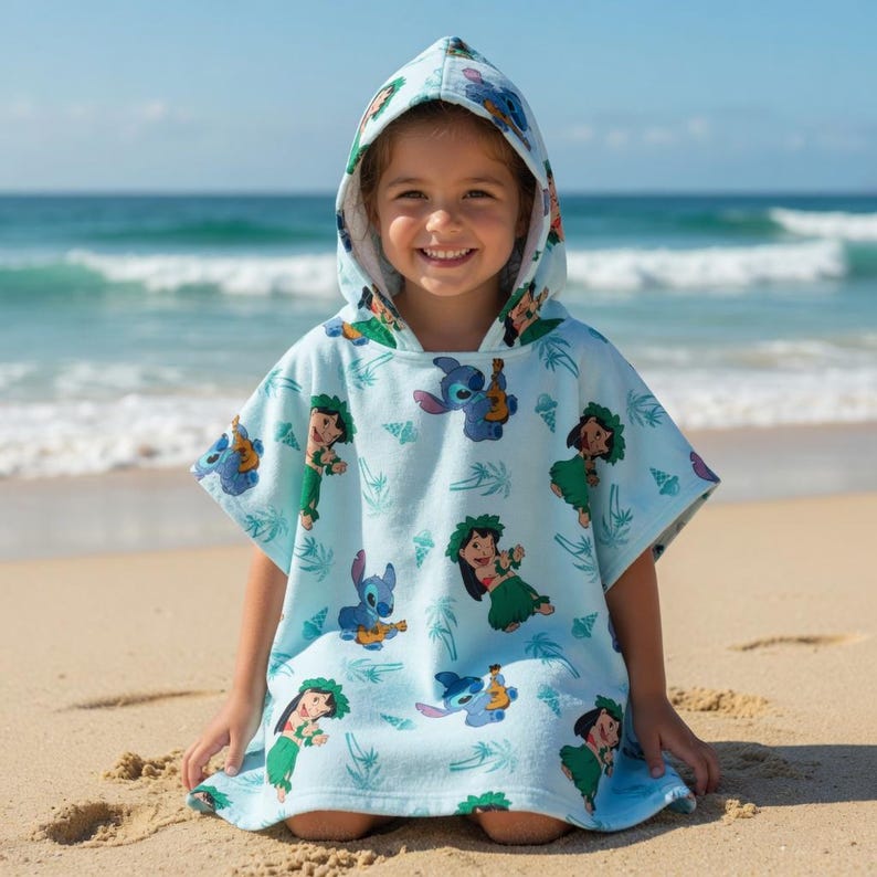 May include: A light blue hooded poncho towel featuring an all-over print of the character Stitch playing a ukulele and a character wearing a green hula skirt, interspersed with small palm tree and seashell illustrations across the fabric.