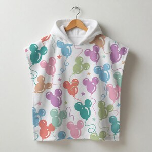 May include: White hooded towel featuring a pattern of mouse-head-shaped balloons in pastel shades of pink, blue, green, orange, and purple. The towel has a hood and is suspended from a wooden hanger.