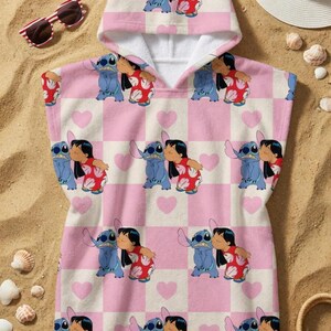 May include: A hooded poncho towel featuring a repeating pattern of Lilo and Stitch characters on a light pink and white checkered background with small pink hearts. The design shows the blue alien and the girl in a red floral dress kissing.