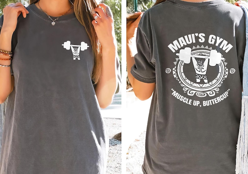 以下が含まれることがあります： 白いウェイトリフターのグラフィックと背面に「Maui's Gym」の文字が入ったグレーのTシャツ。シャツには「Muscle Up, Buttercup」というフレーズも含まれています。シャツの前面には小さなウェイトリフターのグラフィックがあります。