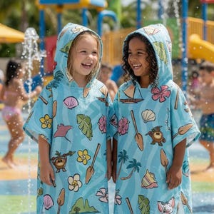May include: Two light blue hooded towels featuring a repeating pattern of tropical motifs including pink hibiscus flowers, seashells, palm leaves, small sailboats, shovels, and cartoon characters, designed with a loose fit and wide sleeves.