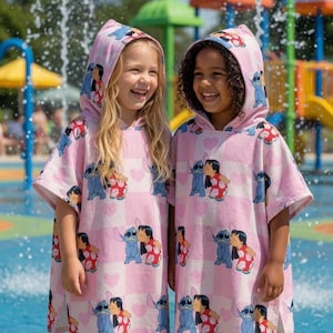 May include: Two hooded poncho towels featuring a repeating pattern of the character Stitch and Lilo on a light pink and white checkered background with small heart shapes. The towels have short sleeves and a loose fit, designed for water activities.