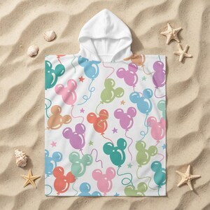 May include: White hooded beach towel featuring a pattern of Mickey Mouse-shaped balloons in shades of pink, blue, green, and orange. The towel is decorated with red stars and curly balloon strings.