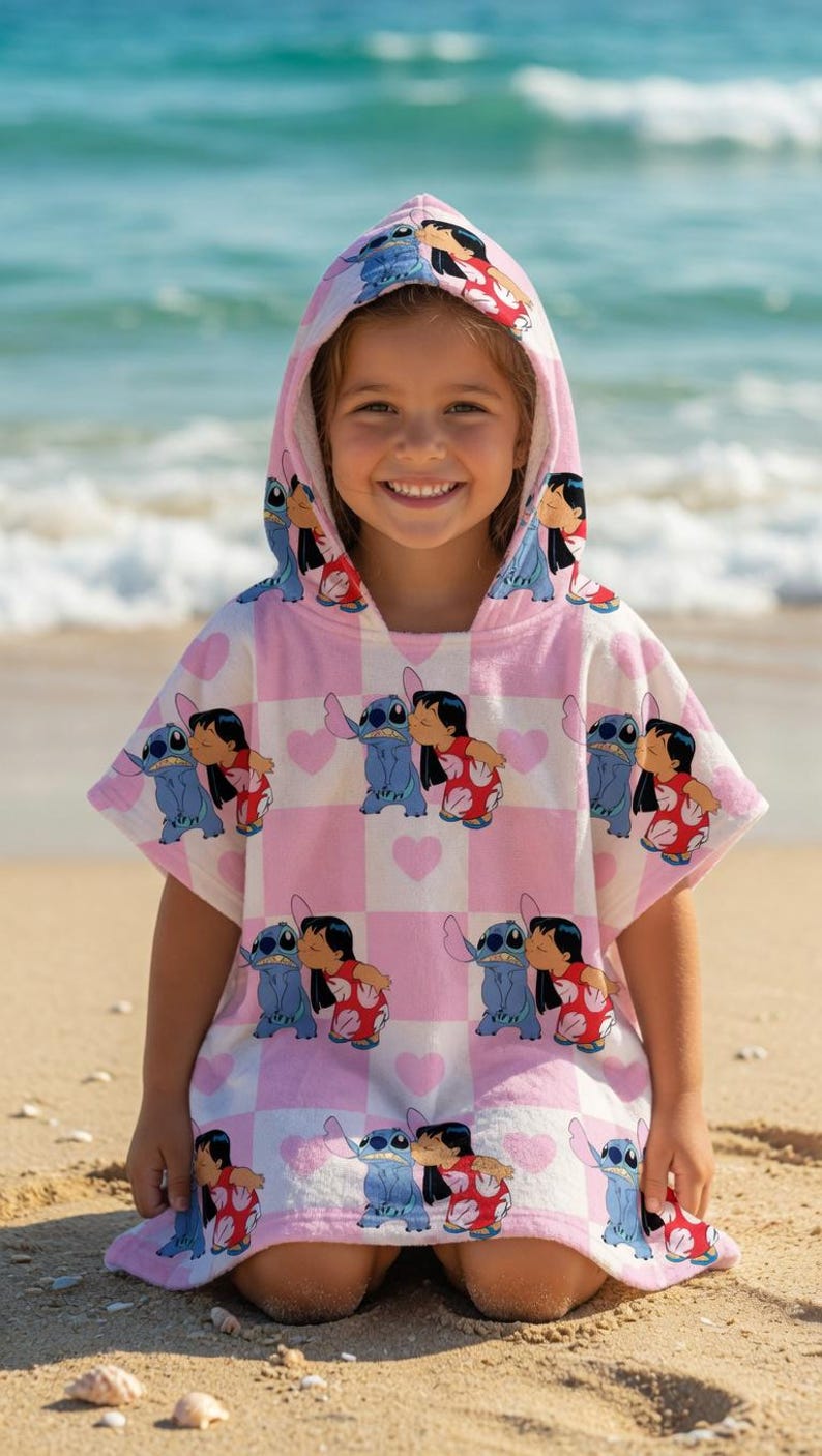 May include: A hooded poncho towel featuring a repeating pattern of Stitch and Lilo on a light pink and white checkered background with small pink hearts. The garment has short sleeves, a hood, and a soft texture, displaying the characters in a kiss.