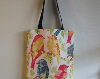 May include: A white tote bag with a colorful bird pattern. The birds are in shades of red, yellow, blue, and orange, perched on green branches with leaves. The bag has a black handle.