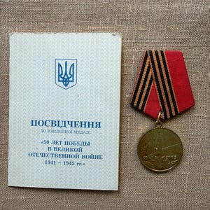 Op de afbeelding: Een ronde bronskleurige medaille met een rood en zwart gestreept lint en een rechthoekig document met een blauw Oekraïens drietand-embleem en cyrillische tekst POSVIDCHENNYA DO YUVIILEINOI MEDALI 50 LET POBEDY V VELIKOI OTECHESTVENNOI VOINE.