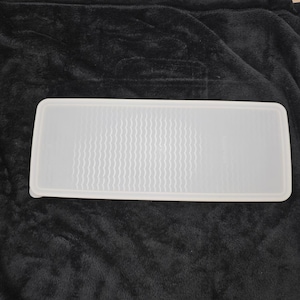 May include: A rectangular, translucent white plastic container lid. The lid has a textured, wavy pattern on the inside surface. The lid is designed to fit a rectangular container.