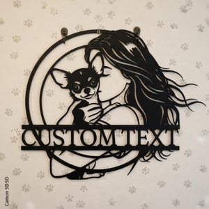 May include: Black metal wall art depicting a woman with a Chihuahua dog inside a circular frame. The design includes the text "CUSTOM TEXT" below the image. The art is designed to be hung on a wall.