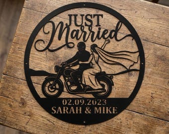 May include: A circular black metal wall sign featuring a cutout silhouette of a couple on a motorcycle. The text reads JUST Married, 02.09.2023, and SARAH & MIKE. The design includes a flowing veil and a motorcycle, framed within a thin circular border.