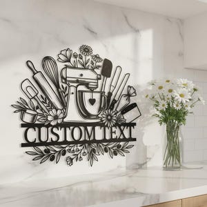 Könnte beinhalten: Ein Wandbild aus schwarzem Metall mit einer Küchenmaschine, einem Schneebesen, einem Nudelholz und verschiedenen Küchenutensilien, umgeben von Blumen- und Blattmotiven, sowie einem horizontalen Balken mit dem Text CUSTOM TEXT.