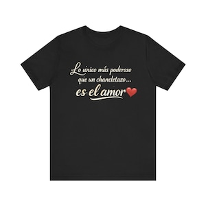 May include: Black t-shirt with the Spanish text "Lo único más poderoso que un chancletazo... es el amor" in a cursive font, with a red heart symbol. The shirt is a crew neck style.