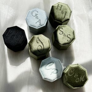 Peut inclure: Plusieurs boîtes à bagues en velours de différentes couleurs, dont noir, bleu clair et vert olive. Chaque boîte octogonale présente des initiales personnalisées brodées sur le couvercle, parfaites pour les mariages ou fiançailles.