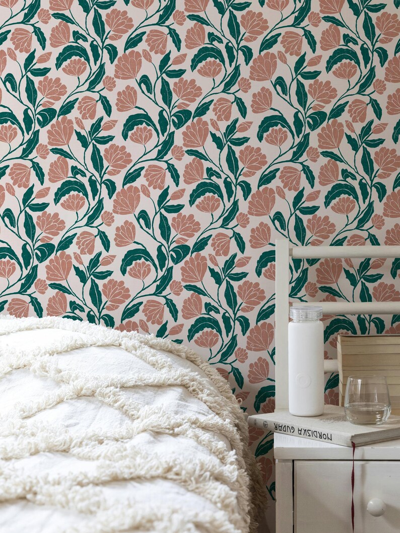 May include: Floral wallpaper featuring a repeating pattern of pink flowers and green leaves on a cream background. The image shows a bed with a white comforter and a nightstand with a water bottle, books, and a glass of water.