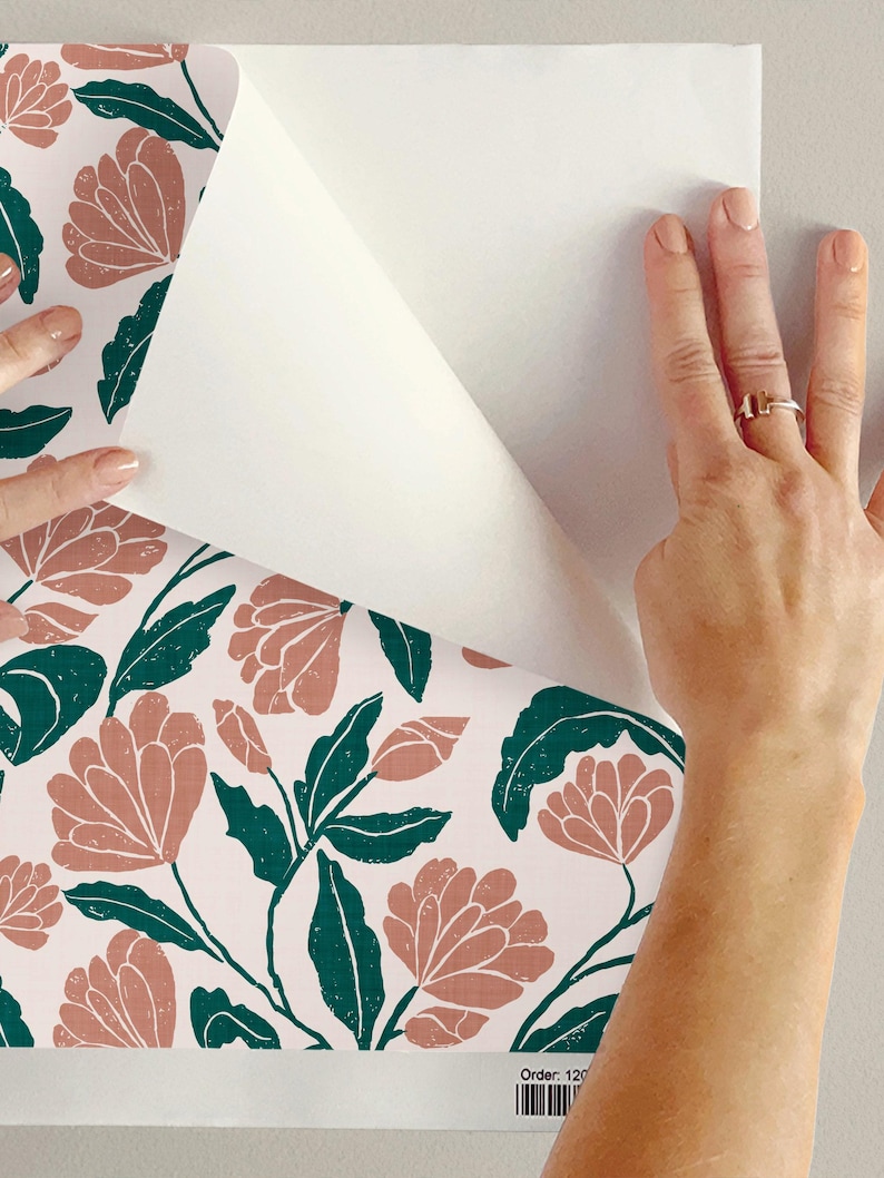 May include: Floral wallpaper with a repeating pattern of coral-colored flowers and dark green leaves on a white background. The wallpaper is being peeled back to reveal the wall behind it.