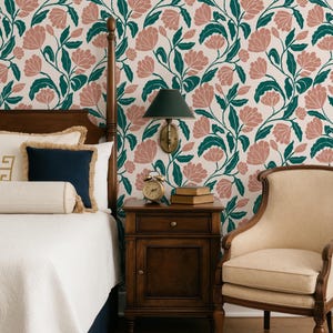 May include: A bedroom scene featuring a floral wallpaper with pink flowers and green leaves. A wooden bed frame, nightstand, and chair are visible. The bed has white bedding and navy blue pillows. A small alarm clock and books sit on the nightstand.