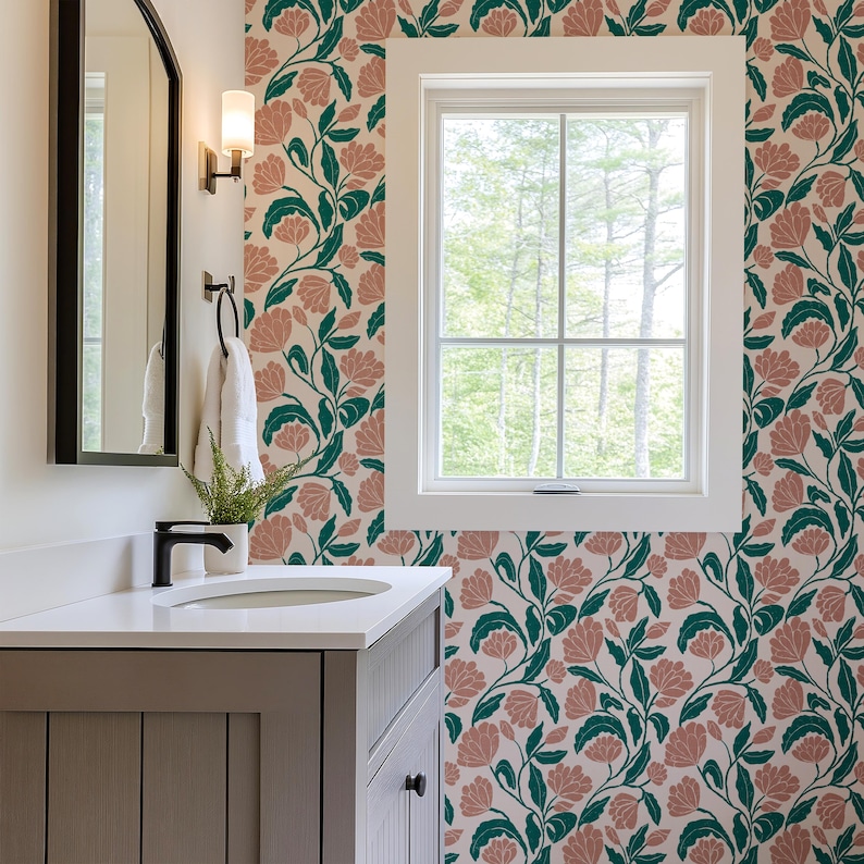 May include: A bathroom with floral wallpaper featuring pink flowers and green leaves on a cream background. The room includes a gray vanity with a white countertop, a mirror, and a window with a view of trees.