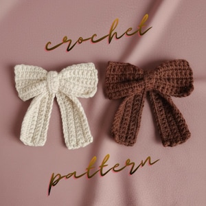 Puede incluir: Dos patrones de lazo de ganchillo hechos a mano en crema y marrón, exhibidos sobre una superficie rosa. Las palabras "crochet" y "pattern" están escritas en escritura dorada. Los lazos están detallados con patrones de puntadas visibles.