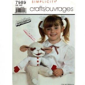 May include: Simplicity crafts pattern 7989 for a Lambchop puppet. The image shows a smiling child with the Lambchop puppet. The puppet is white with red accents on the hands and buttons. The pattern is labeled "ONE SIZE".